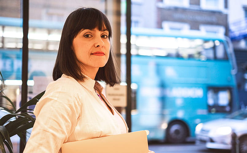 A confident businesswoman holds a laptop while standing in a café