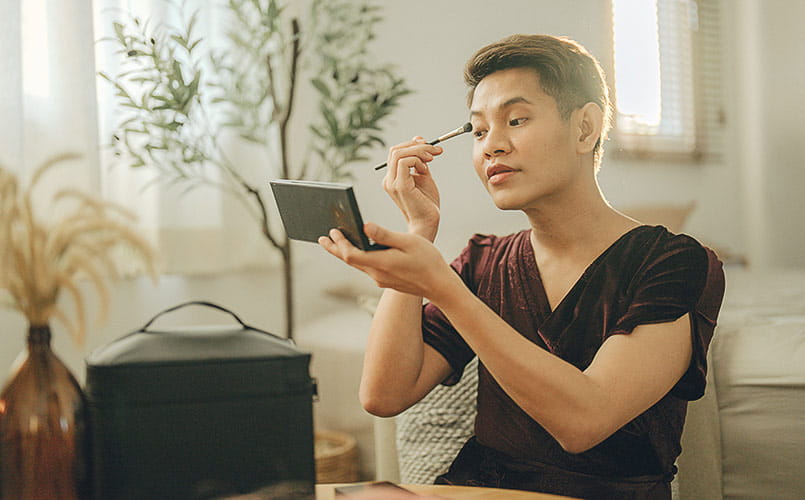 A young transgender man checks their make-up in a handheld mirror