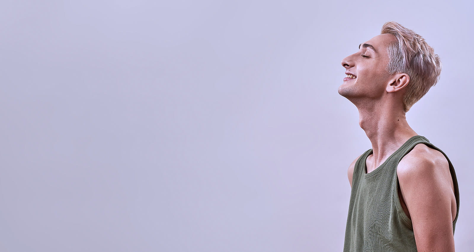 Portrait of a happy androgynous transgender young man lifting head and smiling with eyes closed