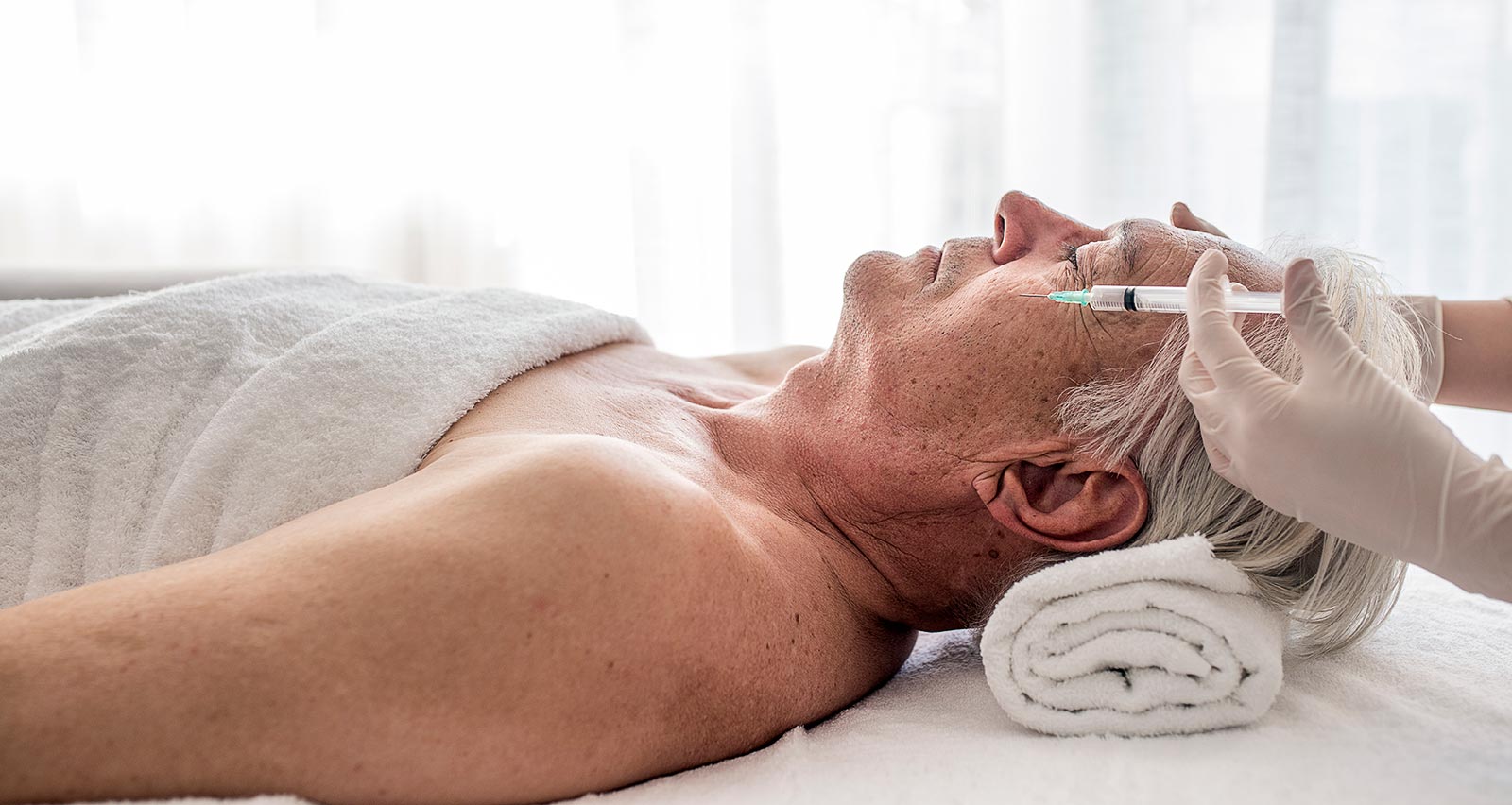  A man laying on table in clinic getting a Botox injection to remove eye wrinkles