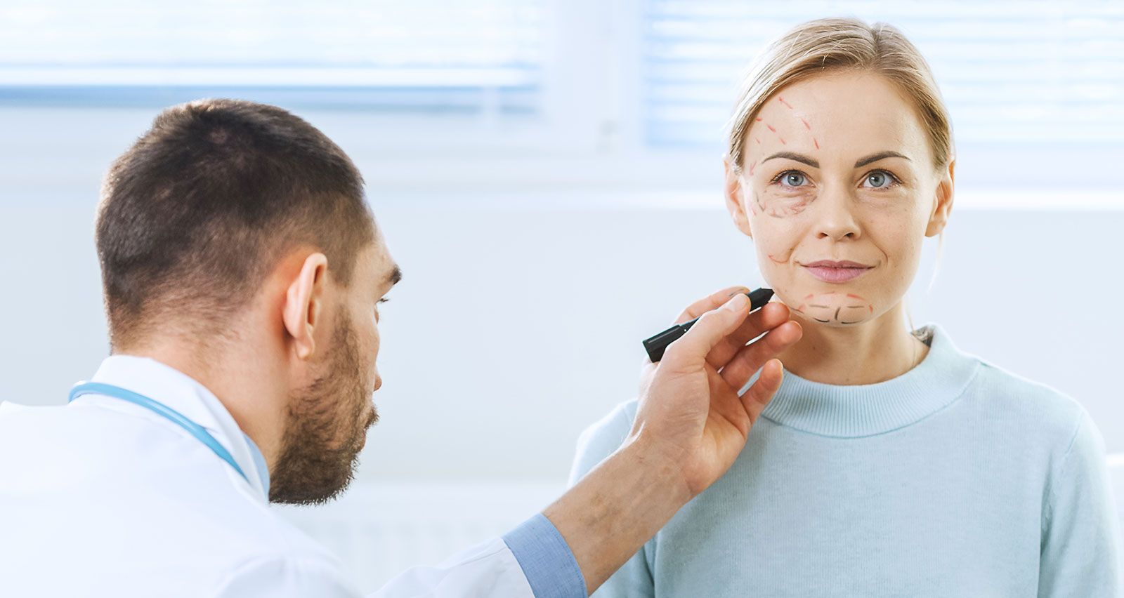 A cosmetic surgeon draws lines on a face of a female patient