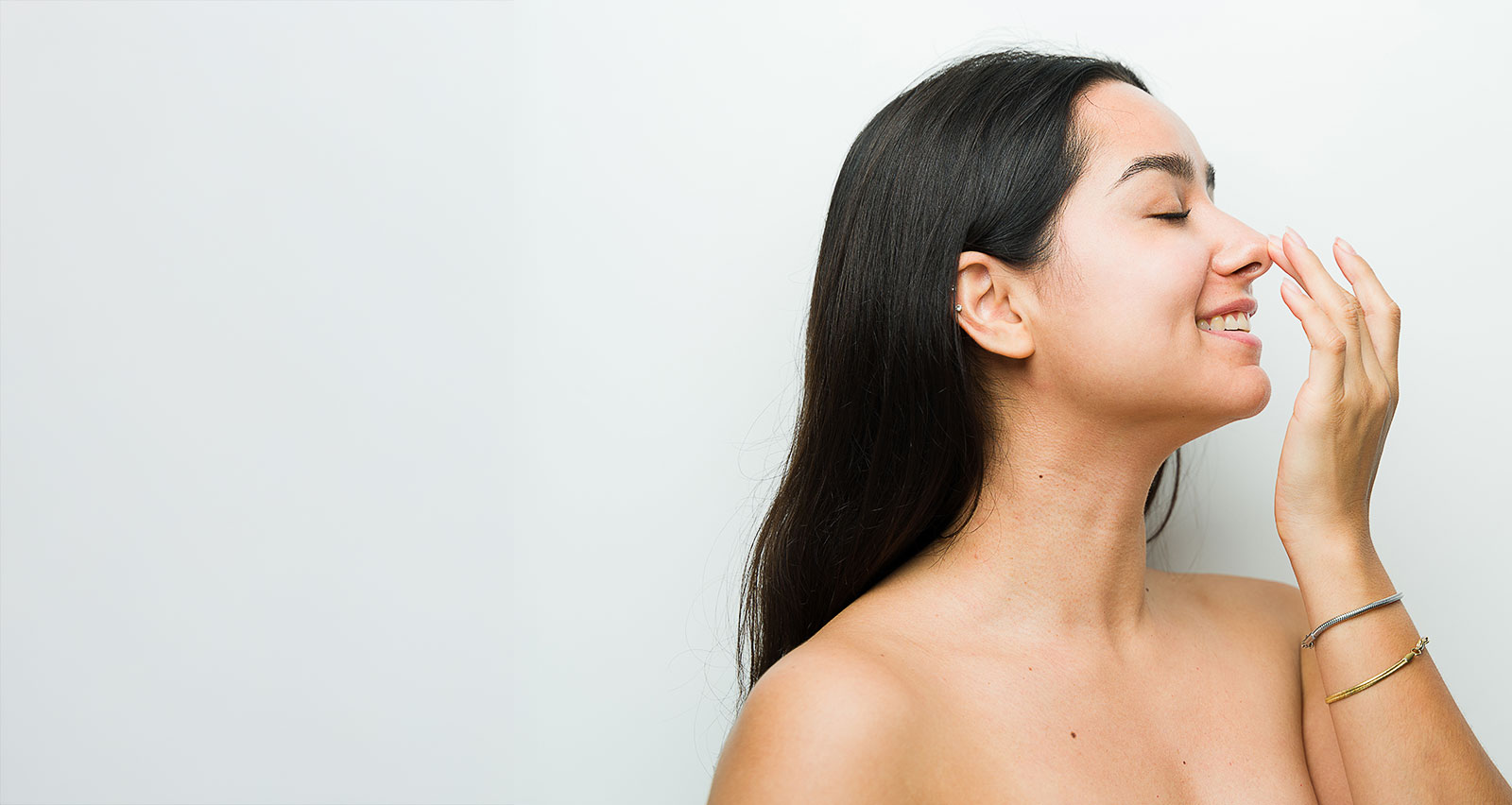A woman in a studio setting touches her nose after a rhinomodelation treatment while looking happy and relaxed