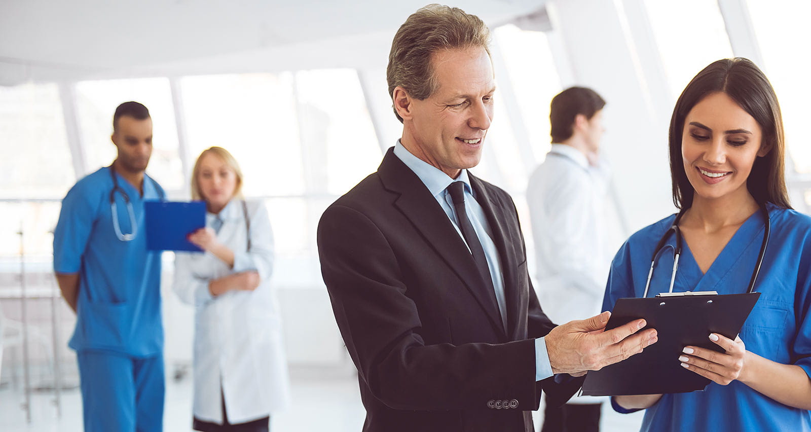 A businessman and doctor are discussing documents and smiling while standing in the hospital hall