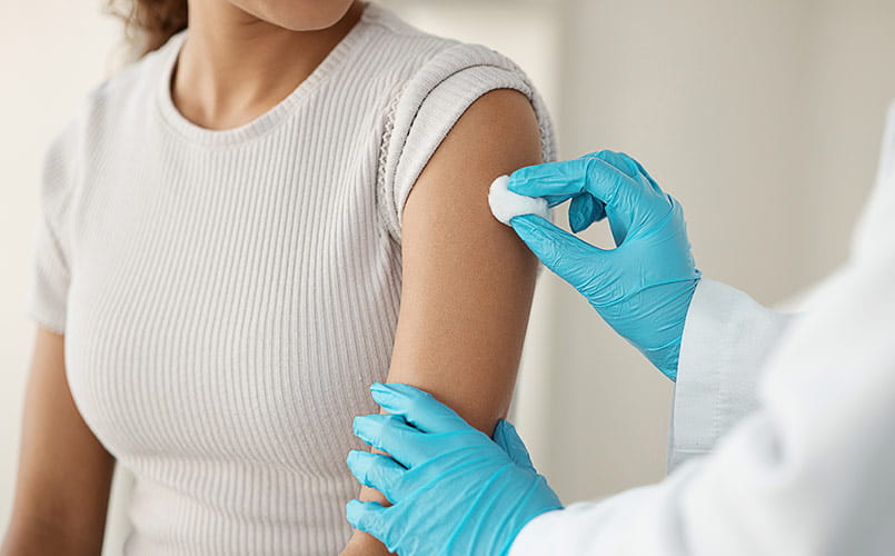 A doctor standing and using a cotton swab on her patient's arm before administering an injection