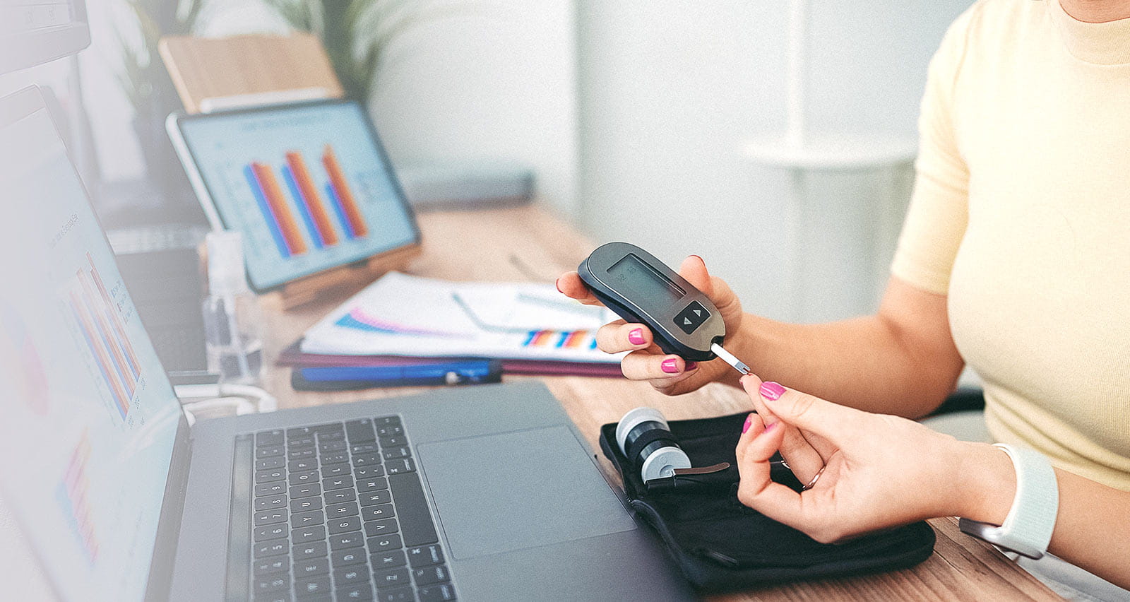 Businesswoman on desk pricks finger with lancing device to monitor blood sugar levels on blood glucose meter