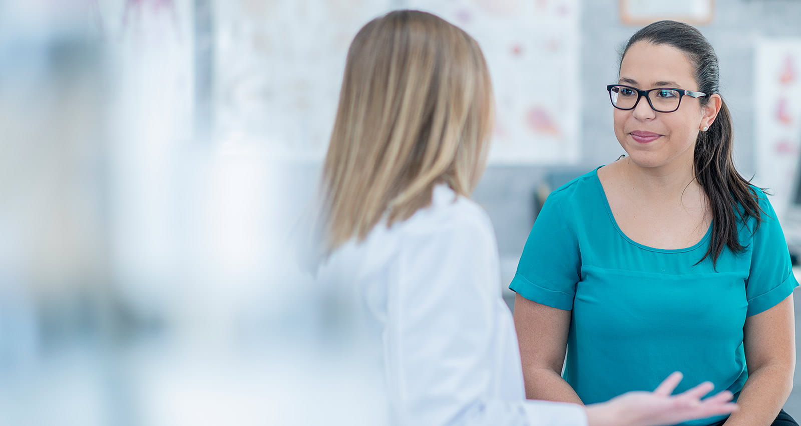 A doctor has her back to the camera while talking to a smiling female patient
