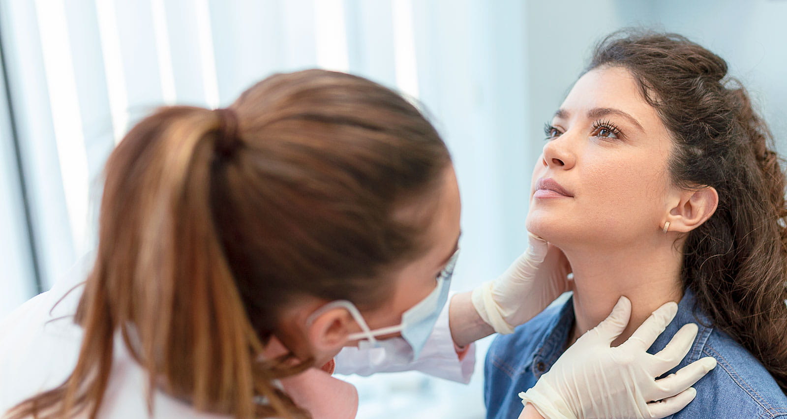 Endocrinologist examining throat of young woman in clinic