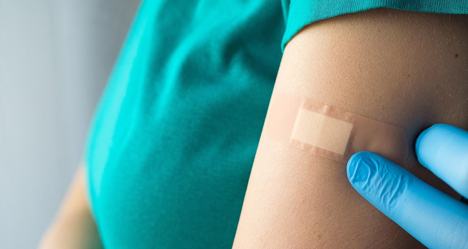 A doctor or health care professional applies a patch or adhesive bandage to a girl or young woman after vaccination
