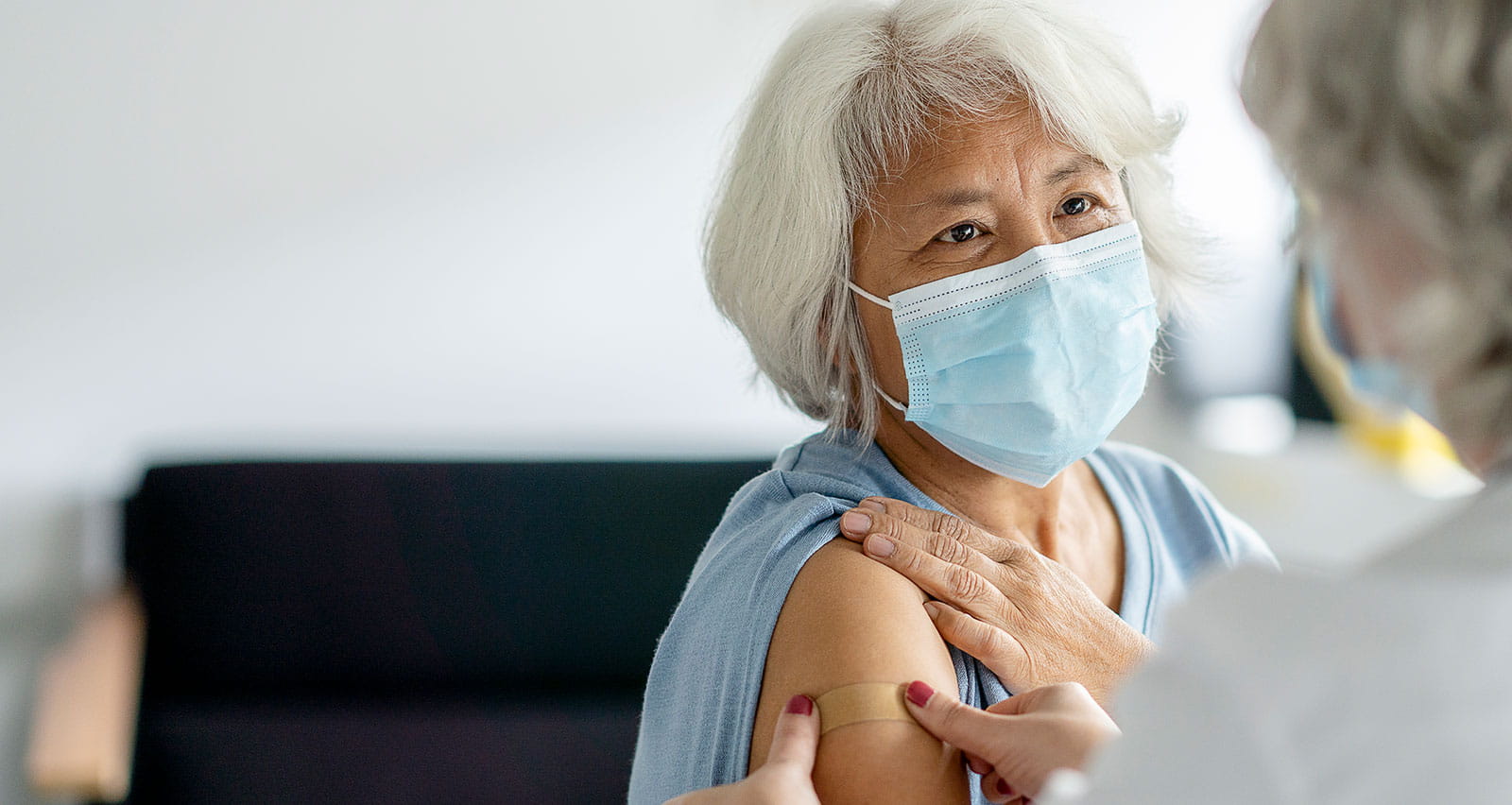 A doctor is putting a bandage on a senior patient's arm after giving her a flu vaccination
