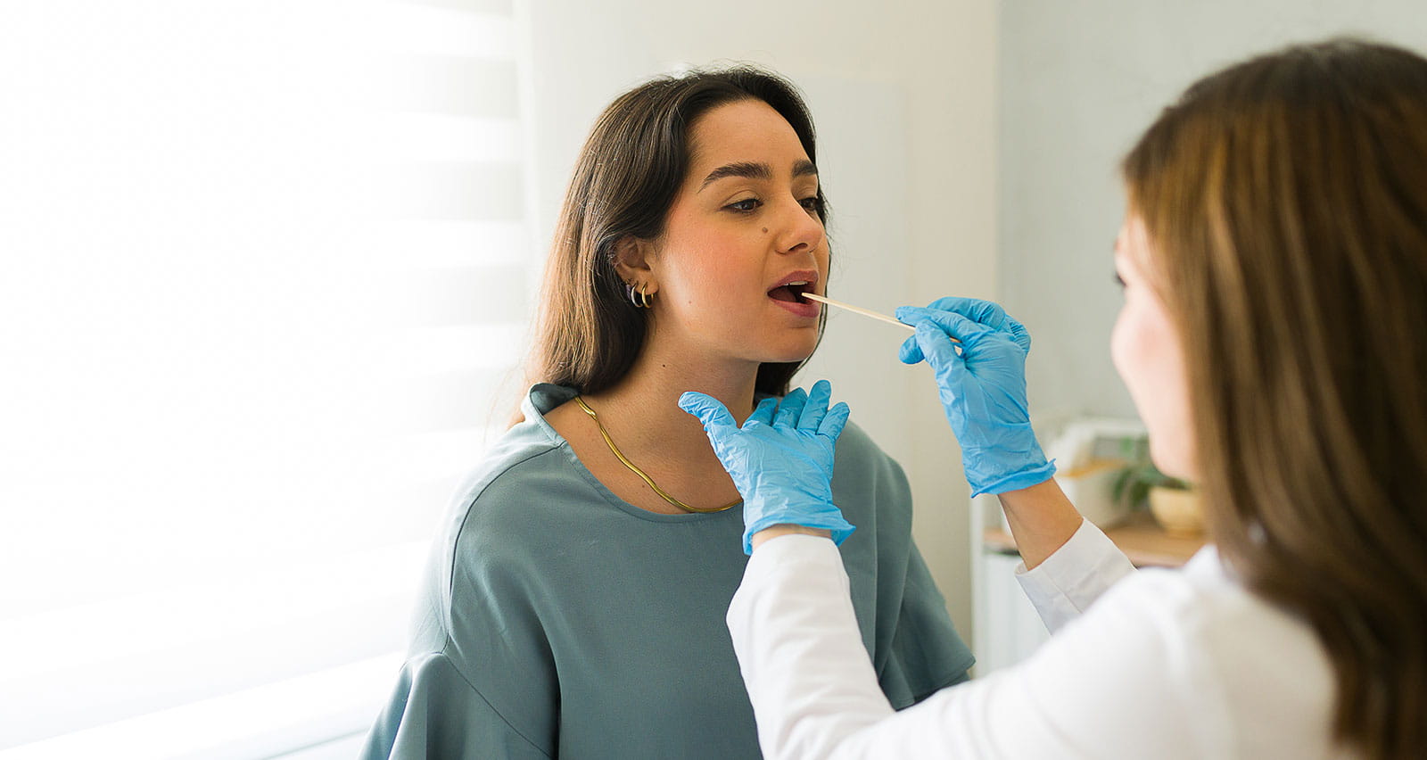 A female doctor wearing blue gloves swabs a patient's throat during a genetics test