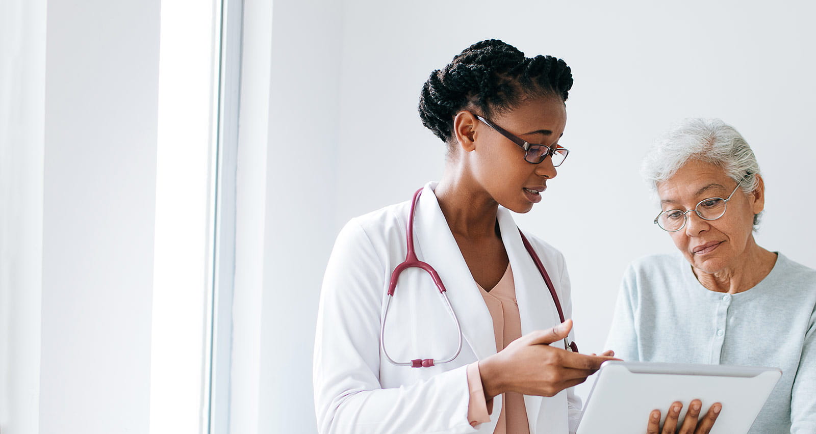 A black female doctor standing next to female patient and showing her something on a digital tablet