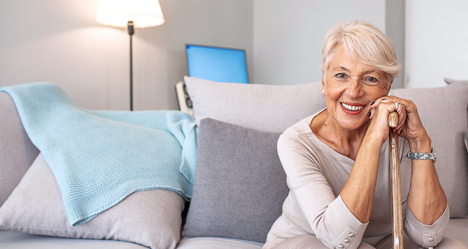 A smiling senior woman with walking cane seated on a sofa