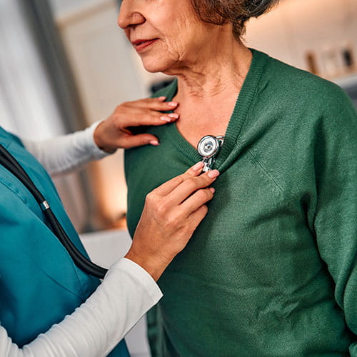 A female doctor holds a stethoscope, listening to the heartbeat of an older female patient