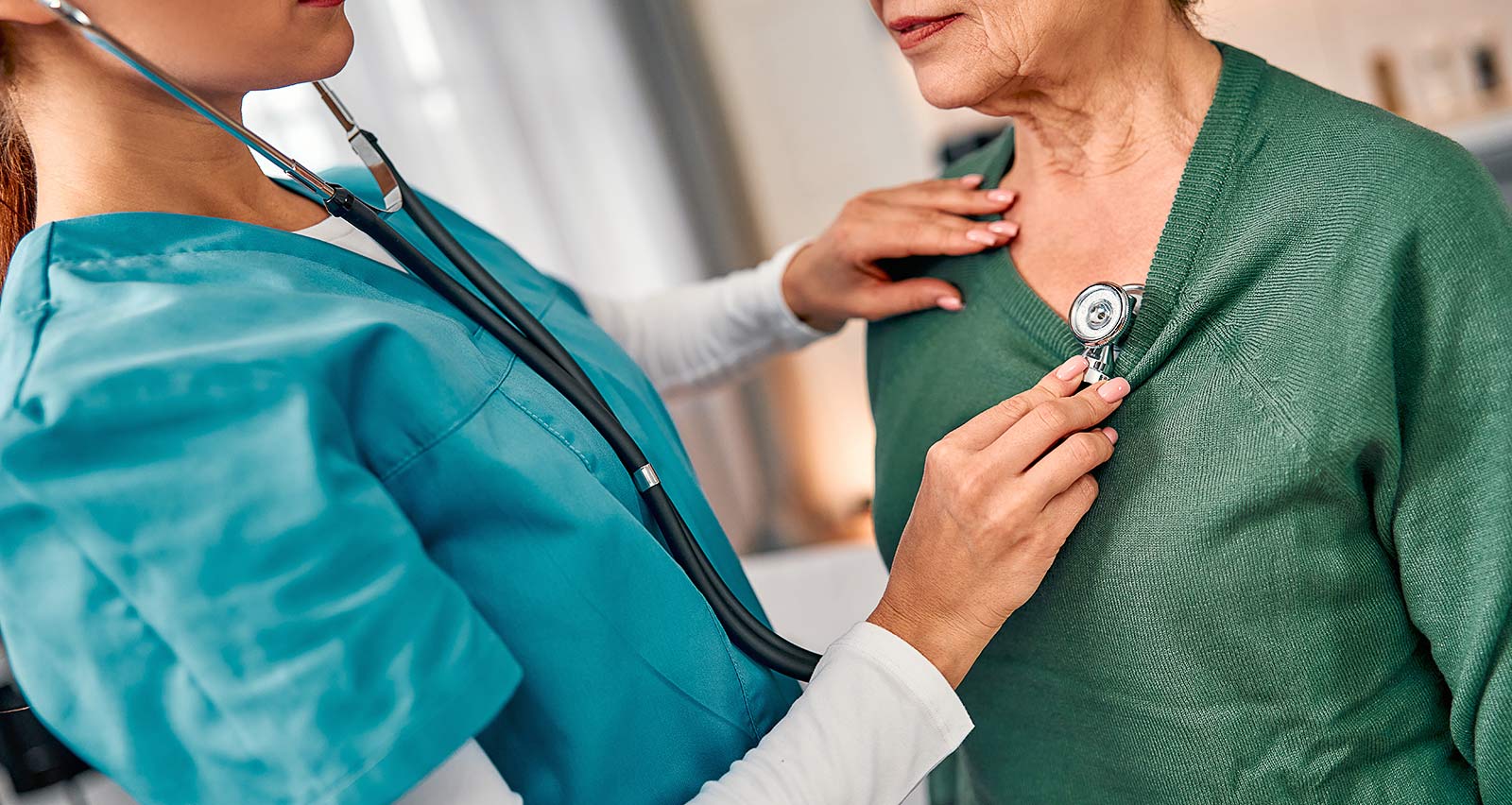 A female doctor holds a stethoscope, listening to the heartbeat of an older female patient