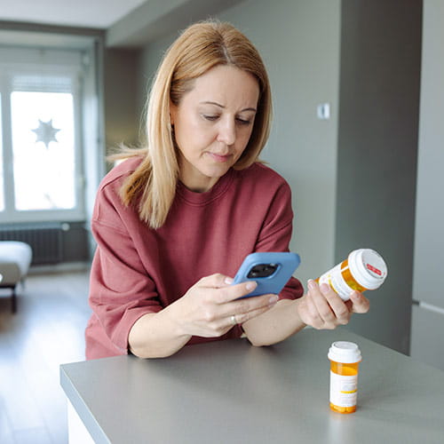 A woman holds a smartphone and a pill bottle while seated in a contemporary apartment