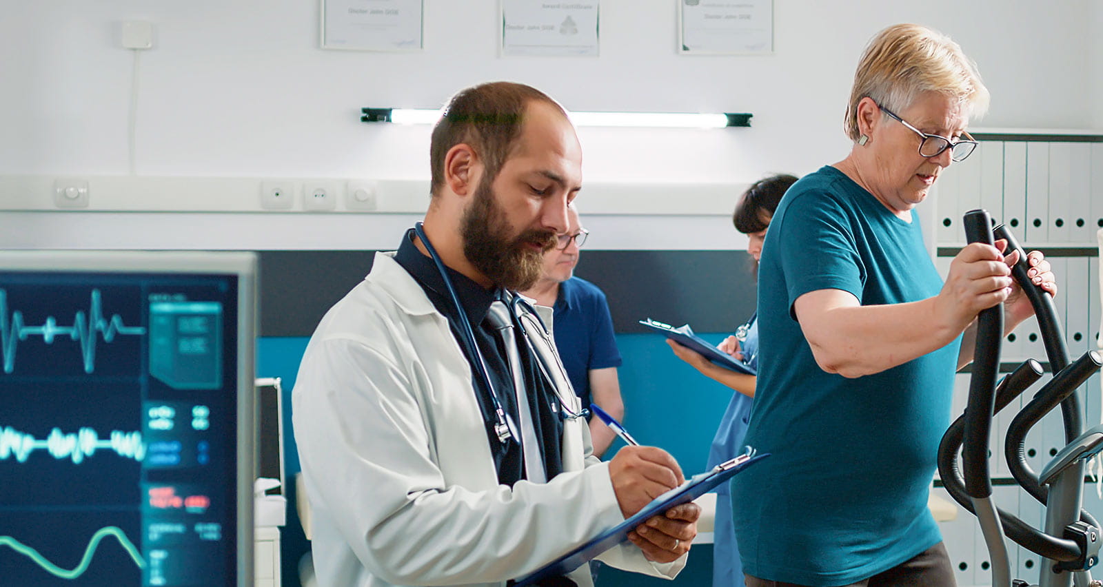 A provider taking notes and watching patient use elliptical machine