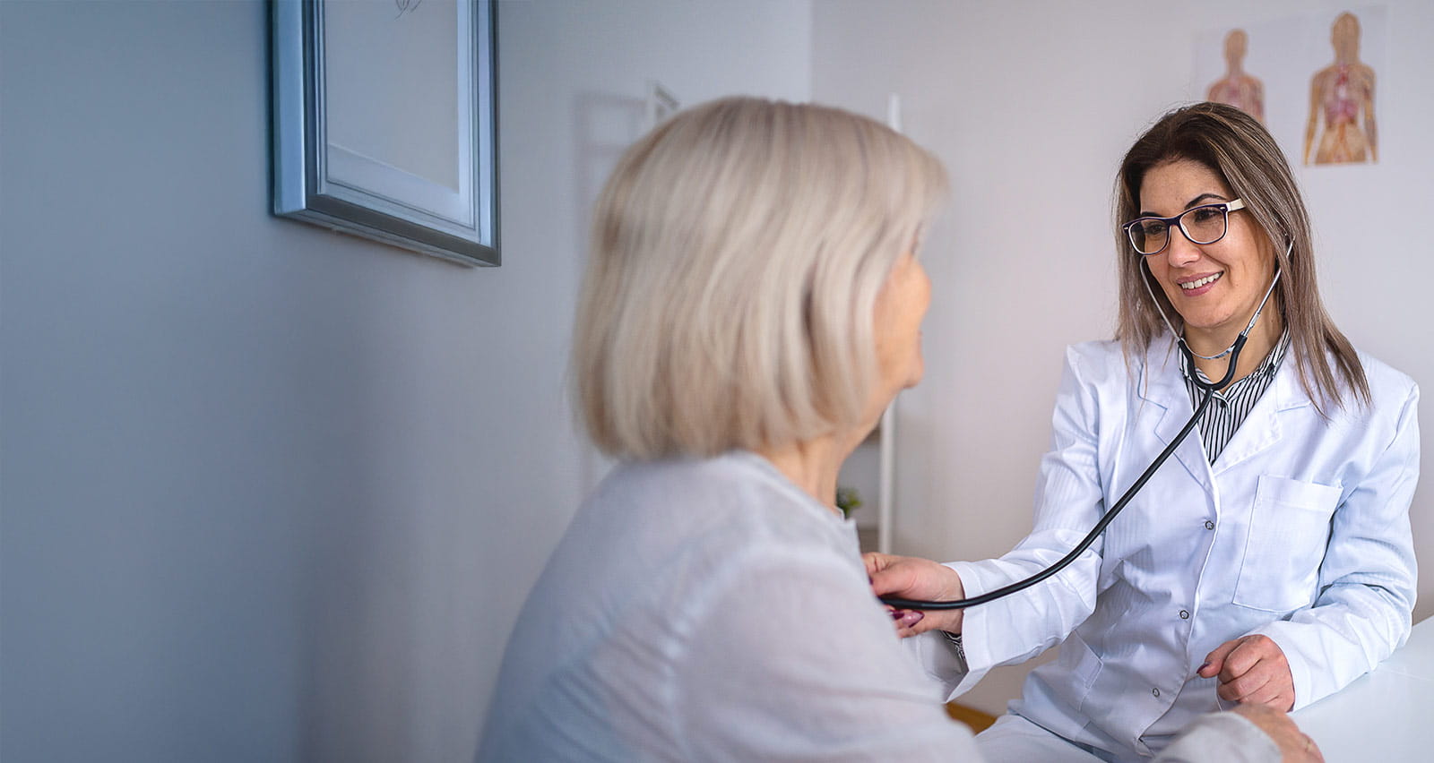 A doctor examines a senior woman’s heartbeat in the exam room