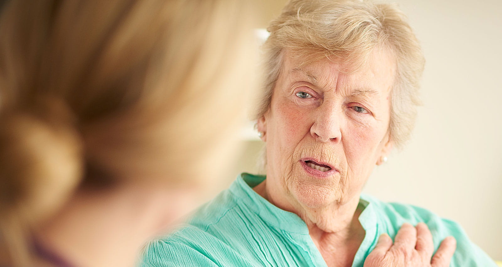 A senior female patient holds upper arm while describing symptoms to a female doctor