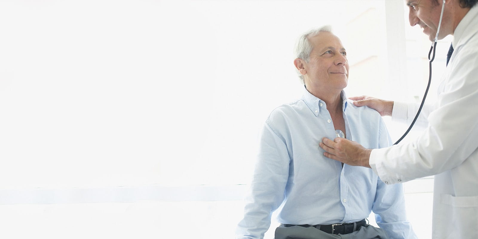 Doctor listening to man's heartbeat in office.