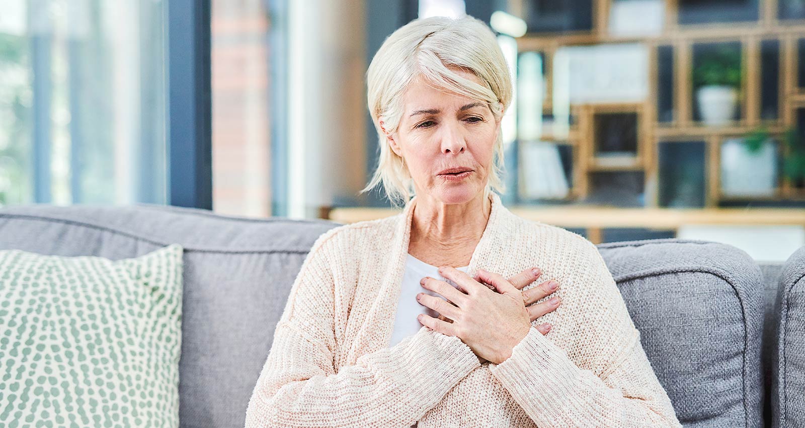 Shot of a senior woman suffering from chest pain while sitting on the sofa at home