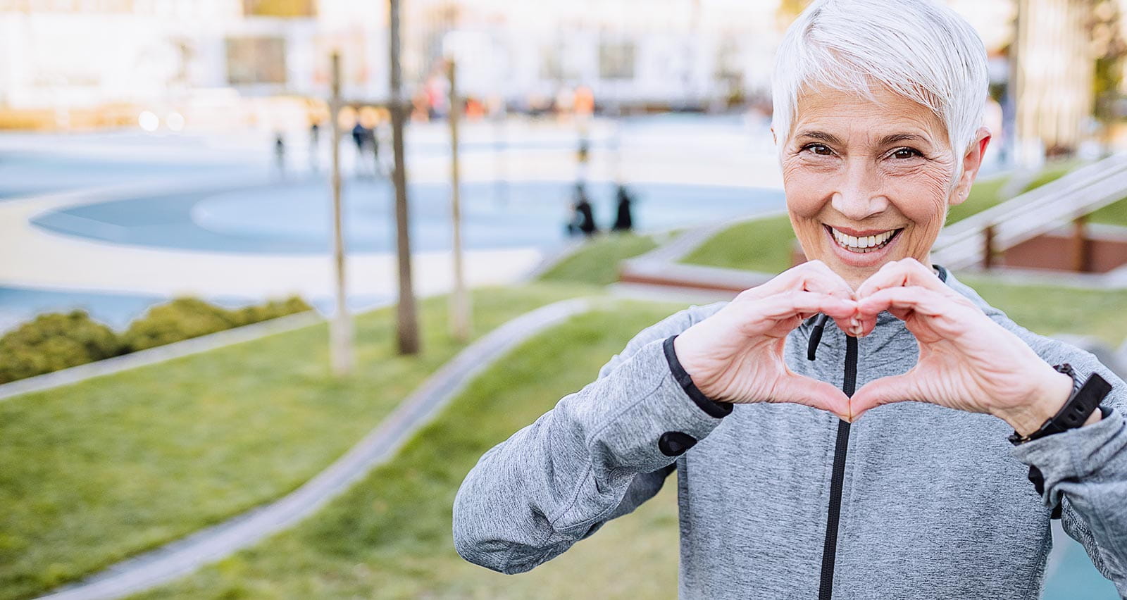 Portrait of a smiling senior woman with short hair wearing sports clothing and making a heart sign with her hands
