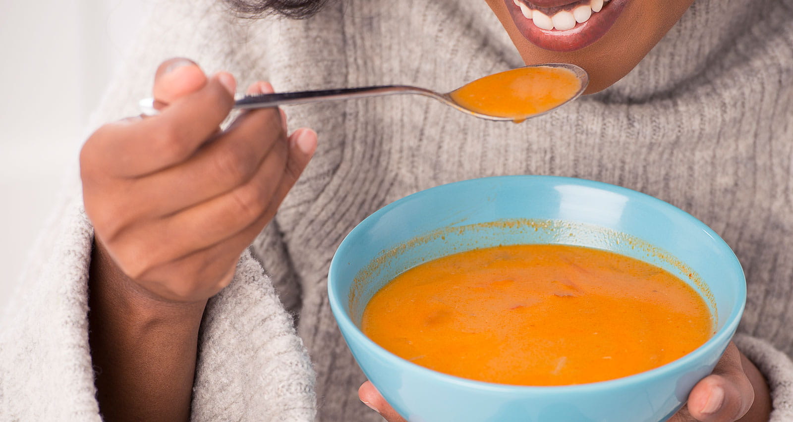 A happy, smiling woman enjoying Thai soup in a blue bowl