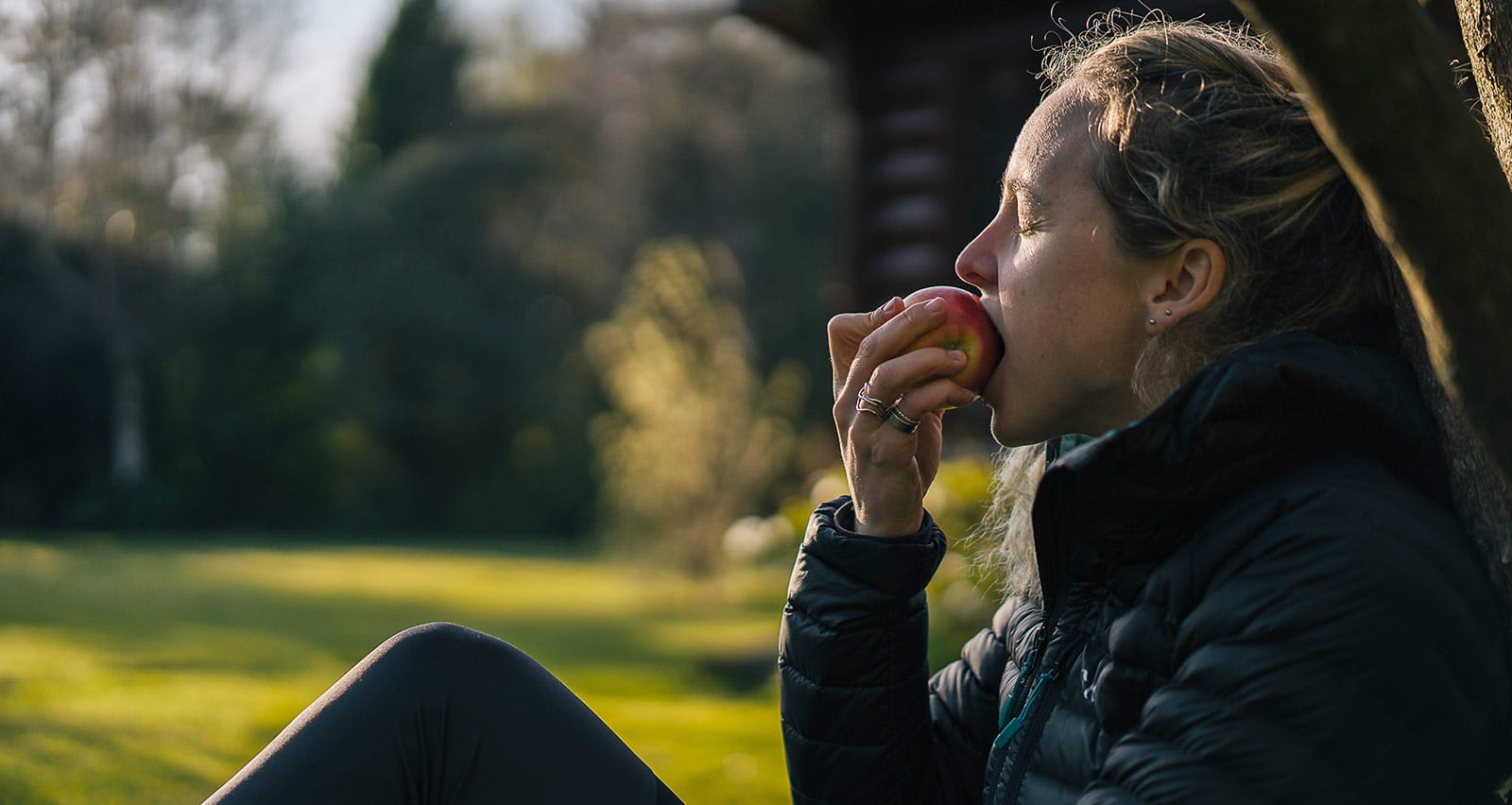 A young woman relaxes in a garden while mindfully eating an apple