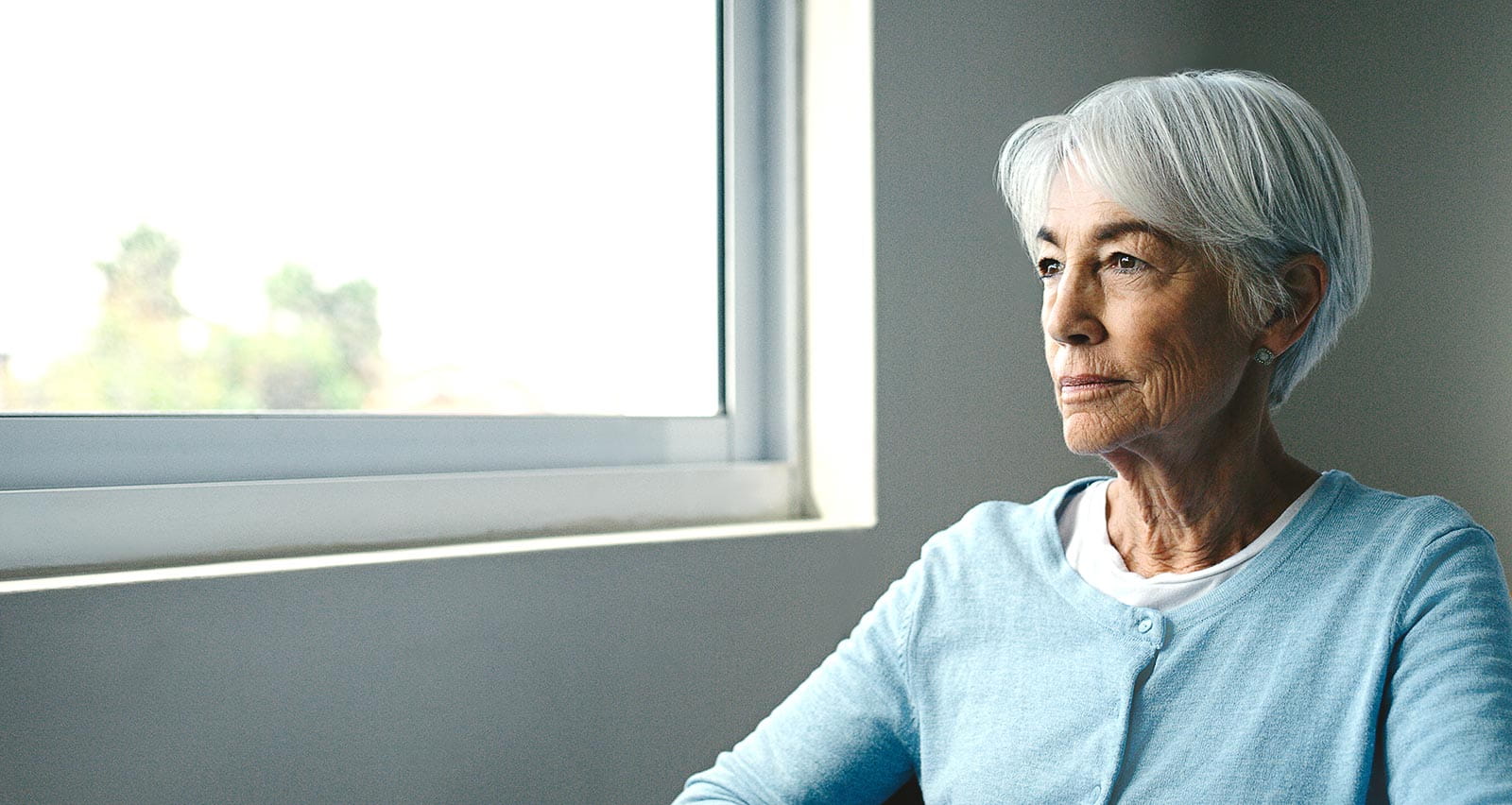 A senior woman in an assisted living facility looks out the window