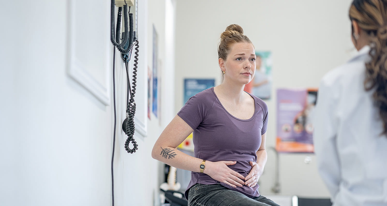 A young woman sits up on an exam table during a medical appointment