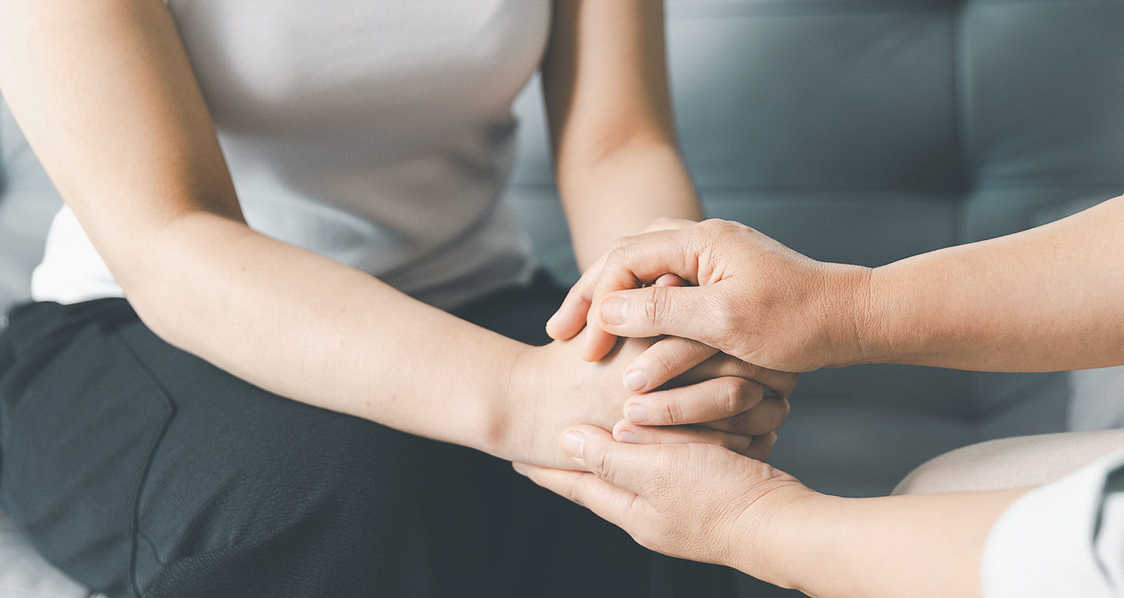 Two women hold hands as a comforting gesture in a therapy session