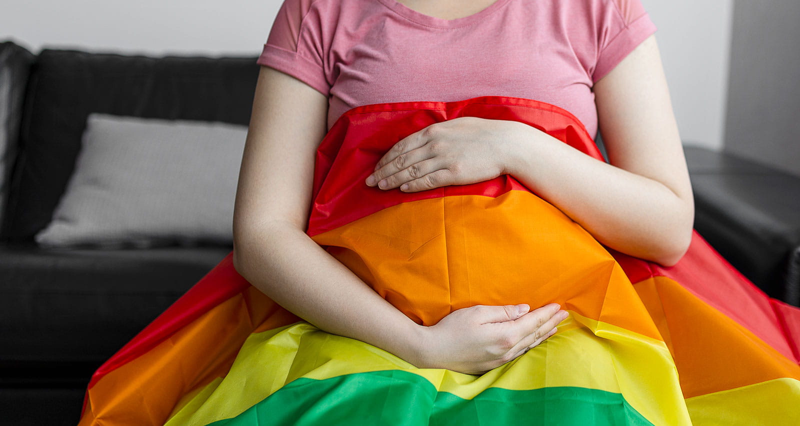 A pregnant woman covers herself with a rainbow flag while seated