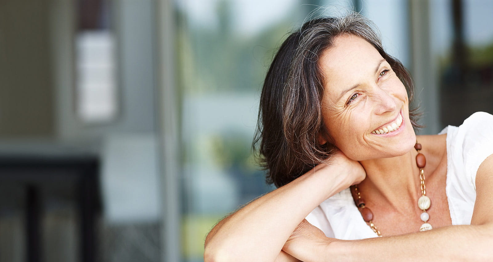 A middle aged woman sitting on ca ouch smiling and looking away