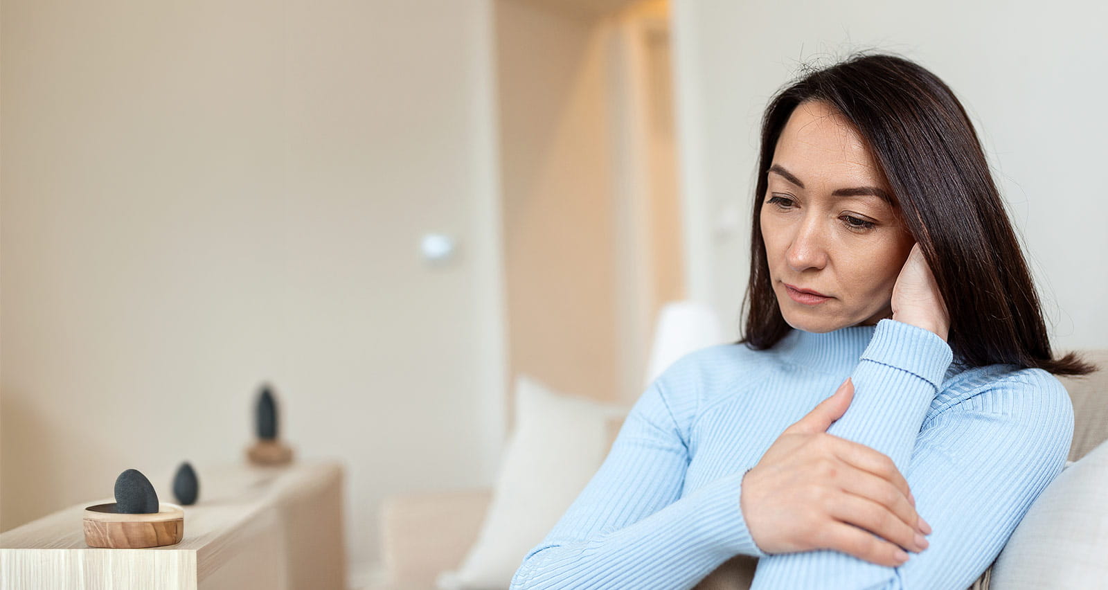 A concerned, tired woman sits alone on her sofa