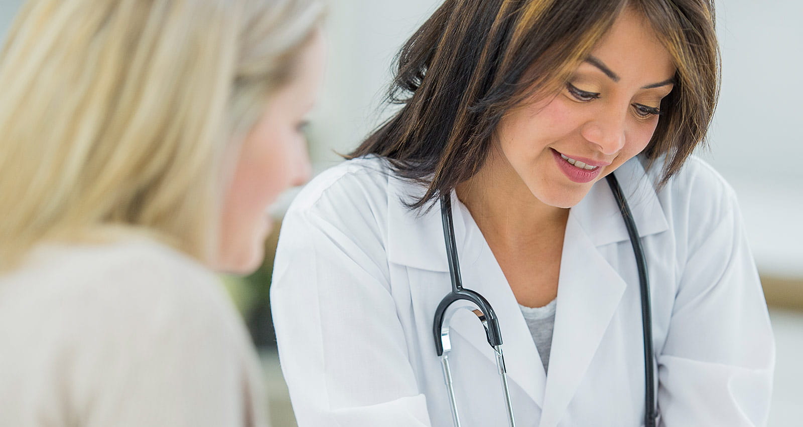 A female doctor consults with her OB-GYN patient, reviewing her medical information on a tablet computer