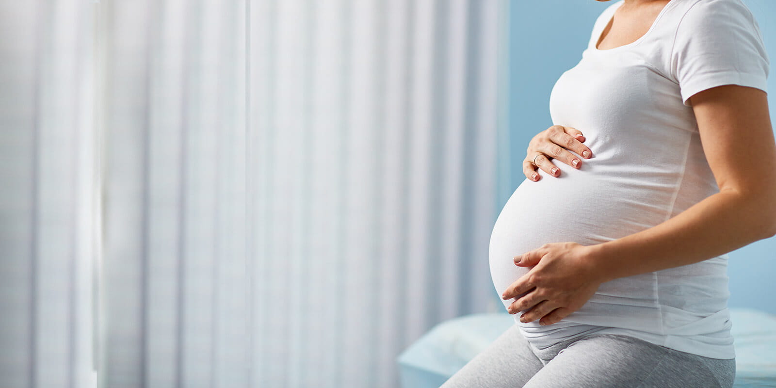 Pregnant woman sitting on hospital bed touching stomach.