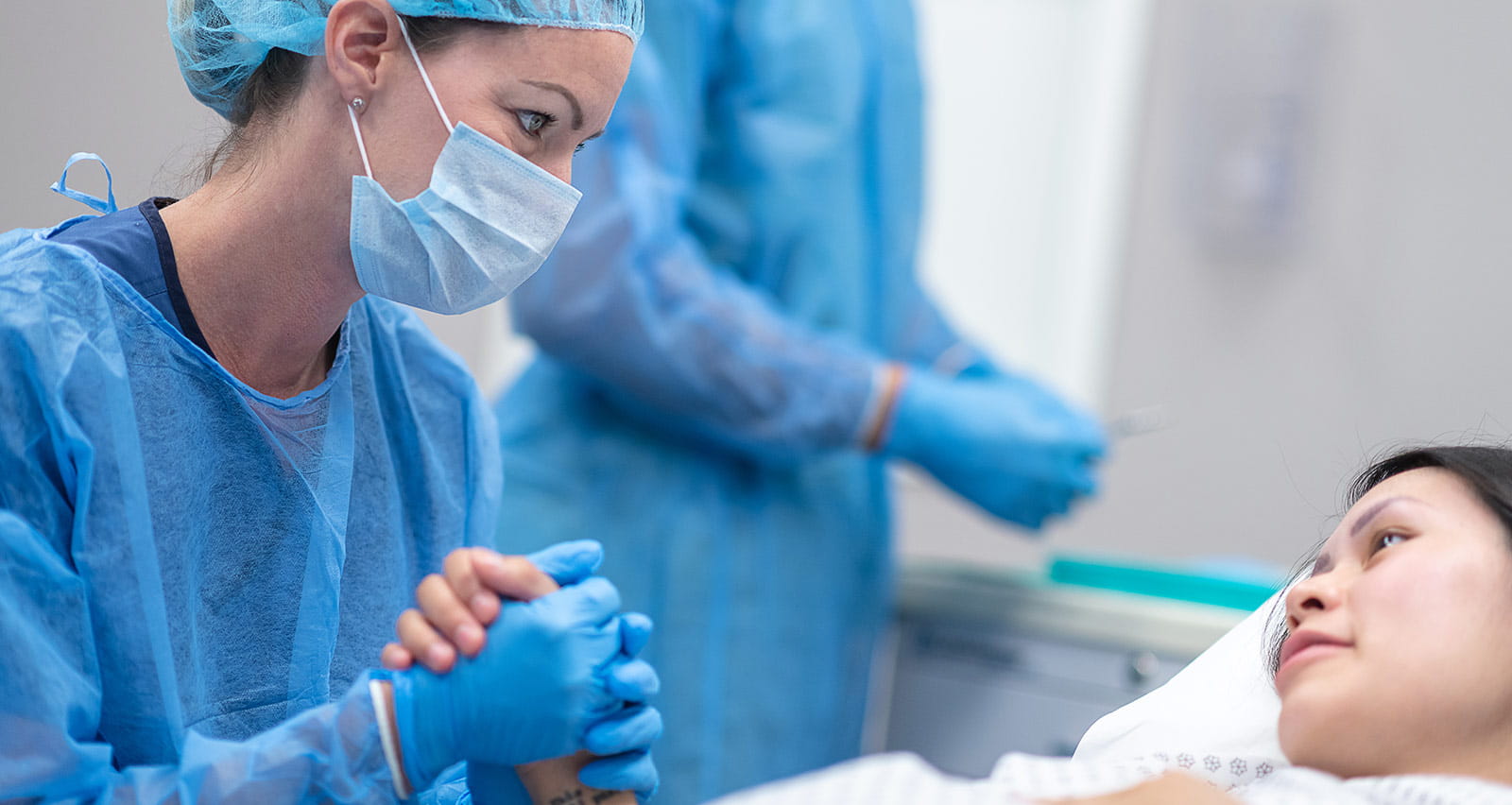 A female surgeon is holding her patient's hand prior to surgery