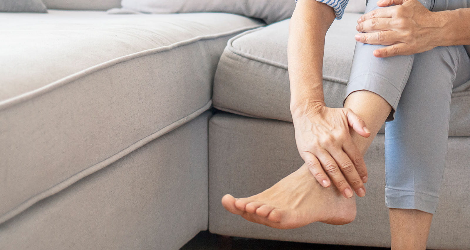 A woman sitting on a couch holds her aching foot