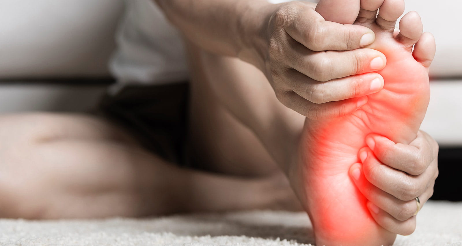 A woman suffering from foot pain uses hand massage to relax the muscles in her right foot