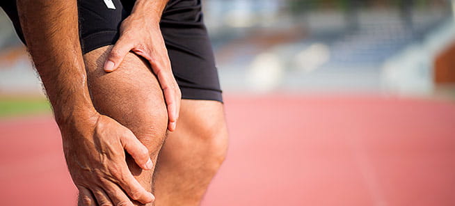 Young sport man with strong athletic legs holding knee with his hands in pain