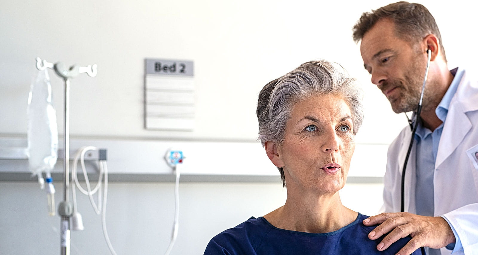 A physician listens to the lungs of a middle-aged woman through a stethoscope