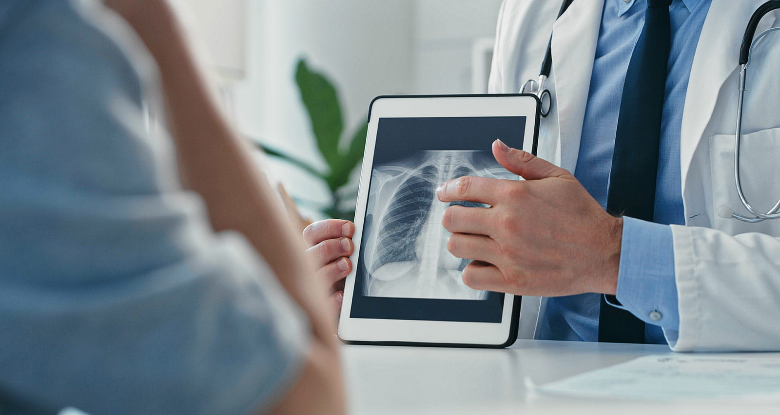 A doctor sitting with his patient and showing her x-rays on a digital tablet