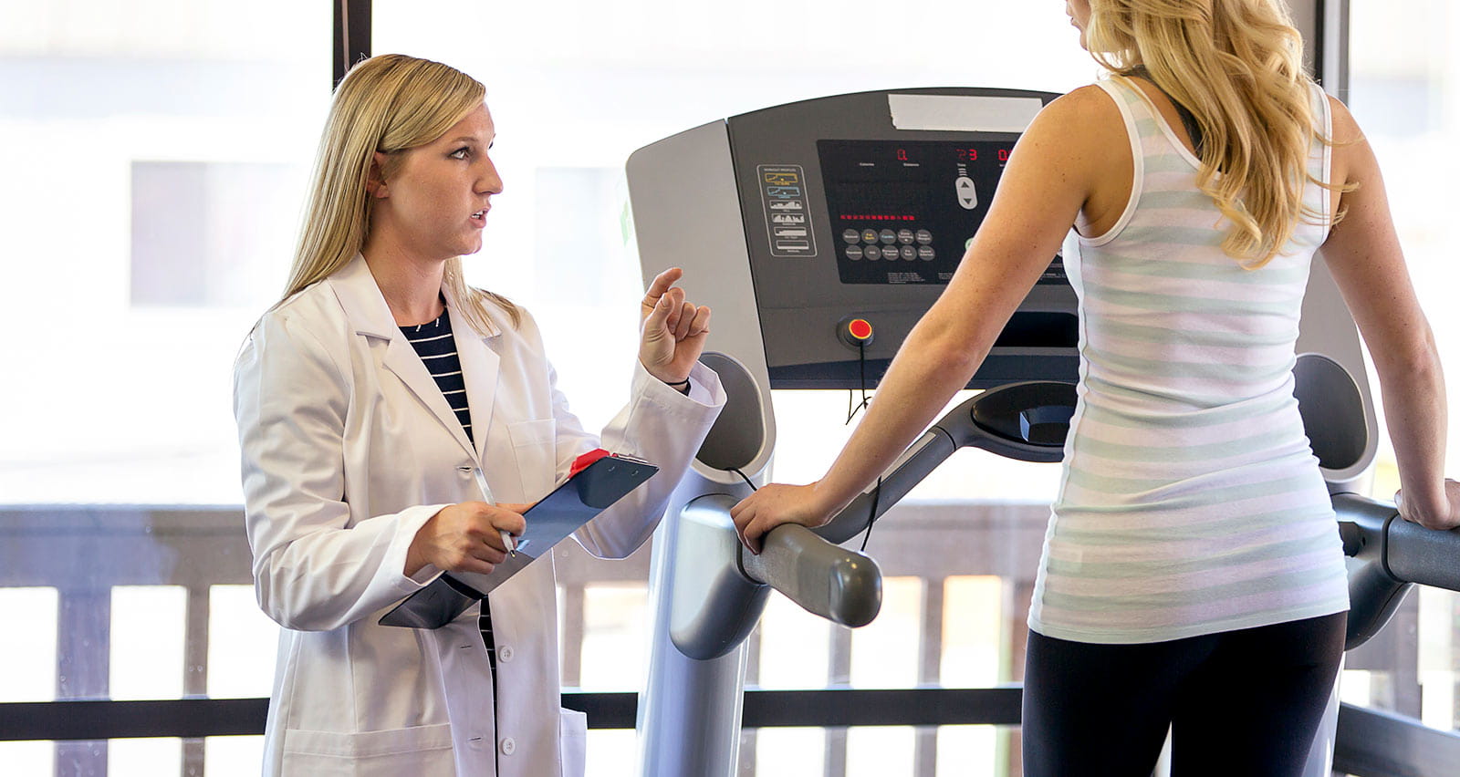 Female physical therapist talking with female patient on treadmill during a rehab session