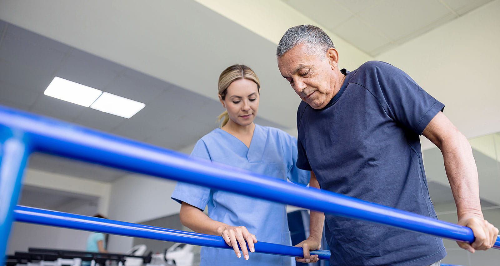 A man doing physical therapy and walking on bars with the assistance of his physical therapist