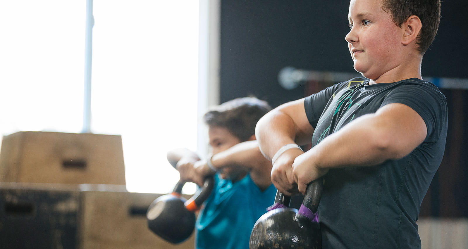 Two young boys lifting kettlebells at a gym
