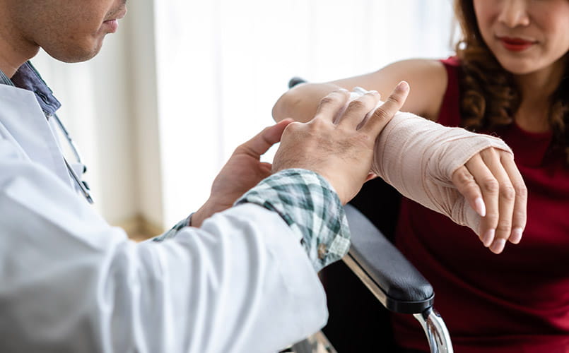 Closeup of doctor wrapping bandages and applying a splint to the arm of a middle-aged female patient