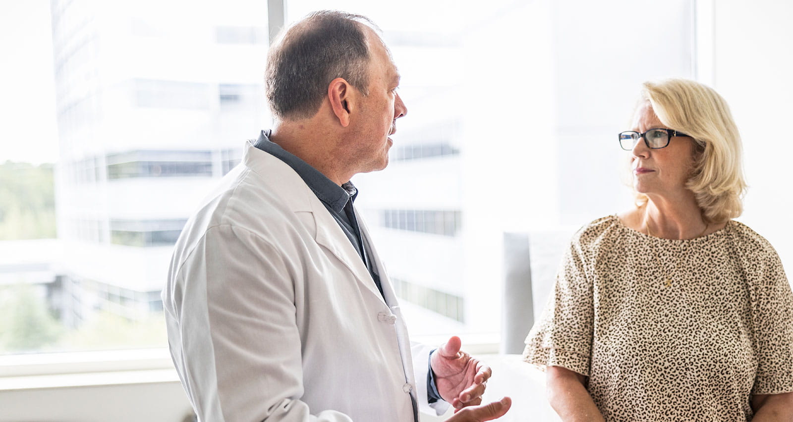 A senior male doctor consulting with a senior woman in an exam room