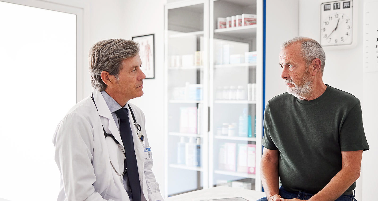 A senior man is discussing treatments with his urologist while sitting on an examination table