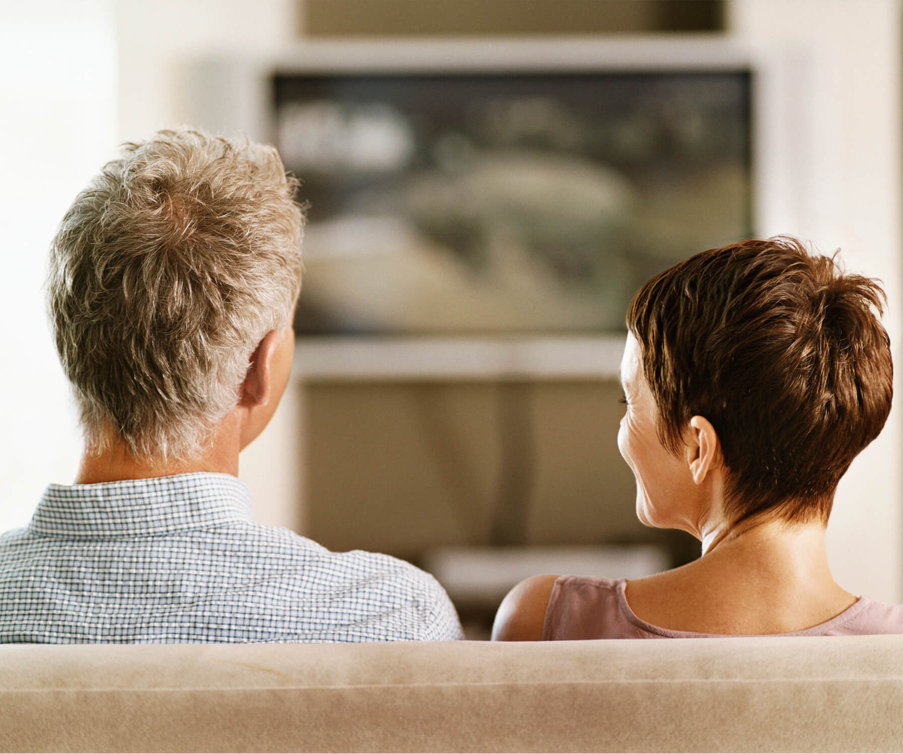 Middle-aged couple sitting in living room watching television