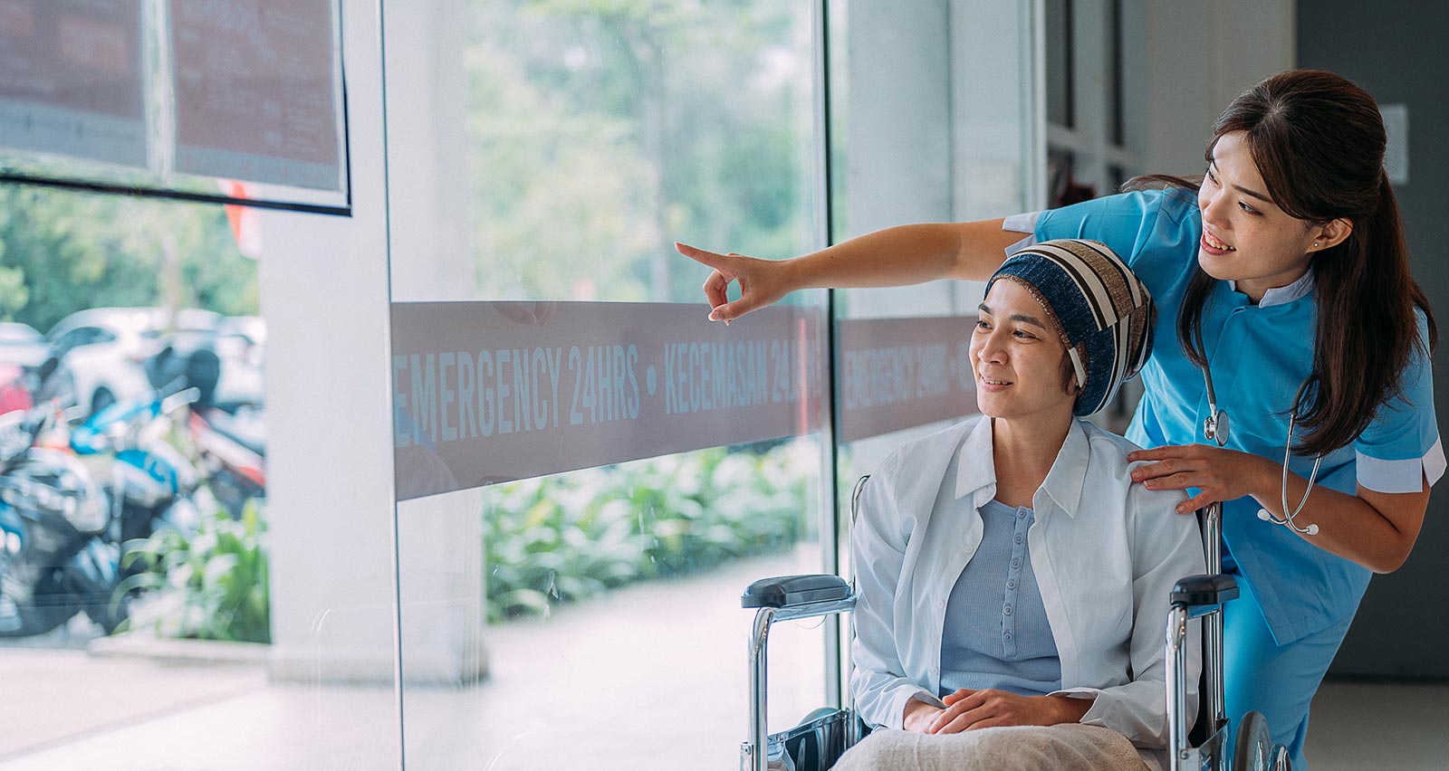 Young female cancer patient in a wheelchair is comforted by female healthcare worker