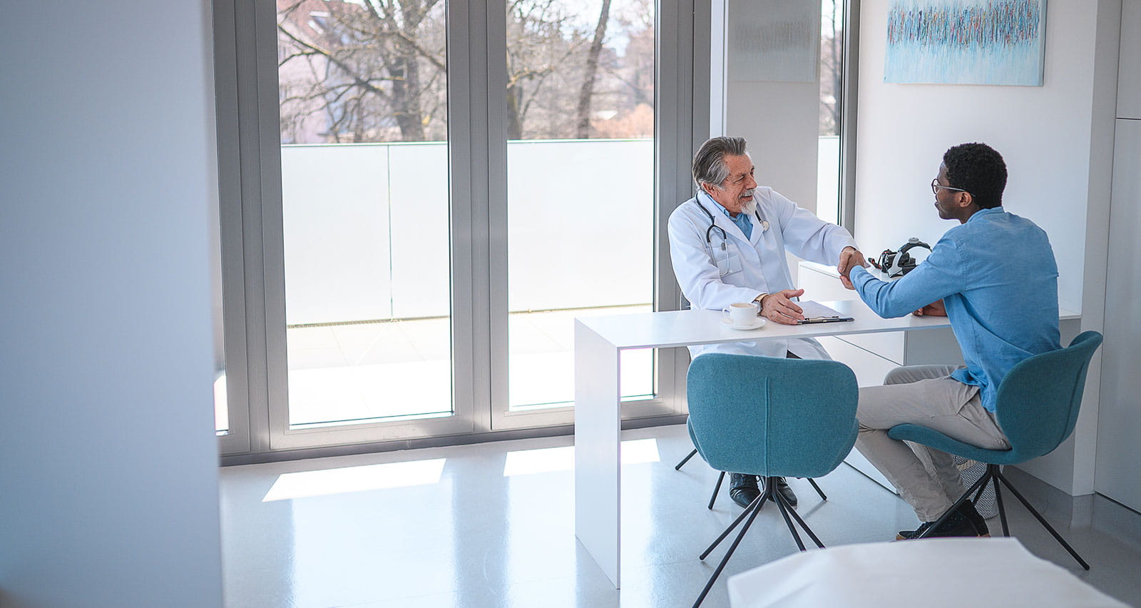A middle aged doctor shaking his male patient’s hand during a consultation